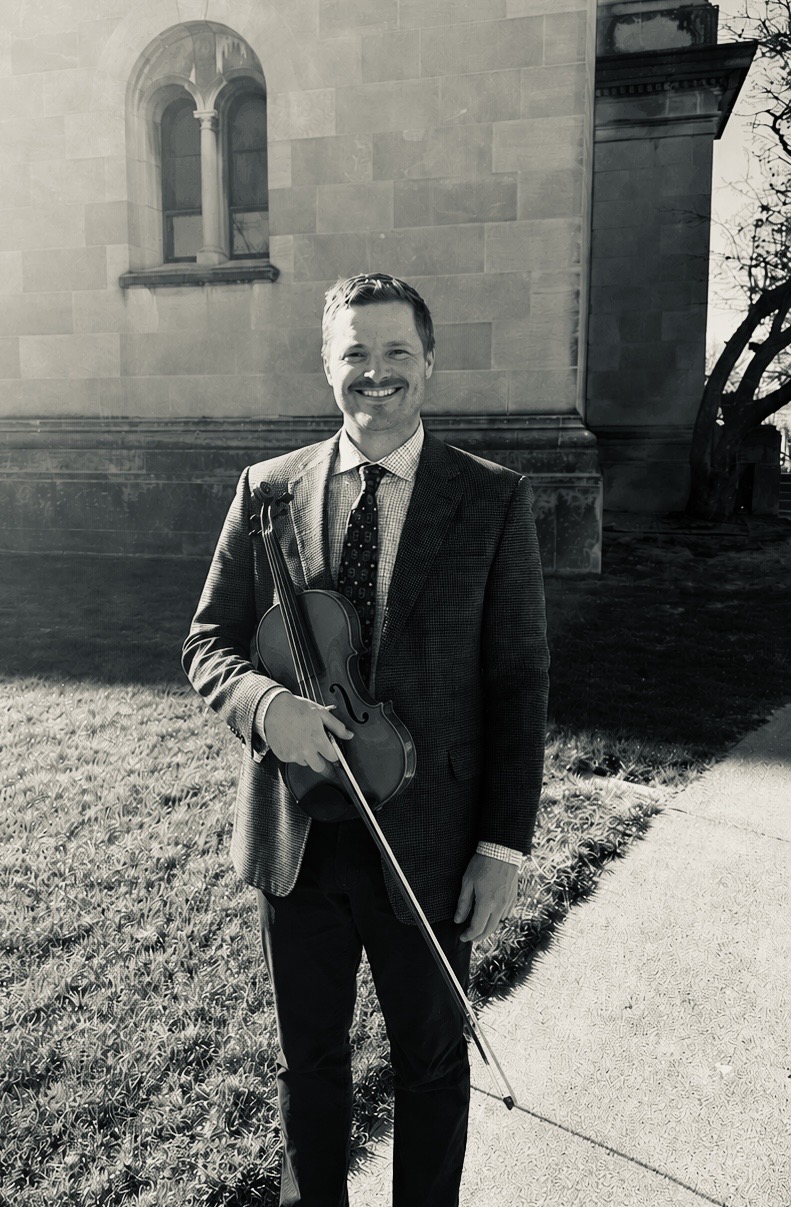 Ryne Bessmer, Omaha wedding violinist, holding violin outside historic stone building